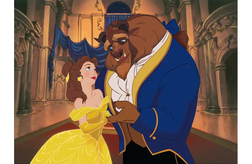 A young woman in a yellow gown smiles while dancing closely with a gentle beast wearing a blue coat in an elegant, ornate ballroom setting.