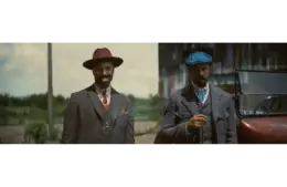 Michael B. Jordan in Golden Globes-winning "Sinners (2025)" as Smoke & Stack in vintage suits stand outdoors near a classic car. The man on the left wears a burgundy hat, while the right wears a blue cap. The scene feels nostalgic.