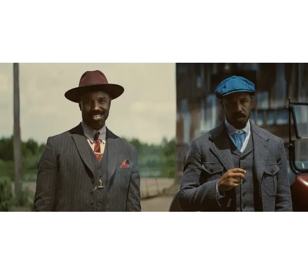Michael B. Jordan in Golden Globes-winning "Sinners (2025)" as Smoke & Stack in vintage suits stand outdoors near a classic car. The man on the left wears a burgundy hat, while the right wears a blue cap. The scene feels nostalgic.