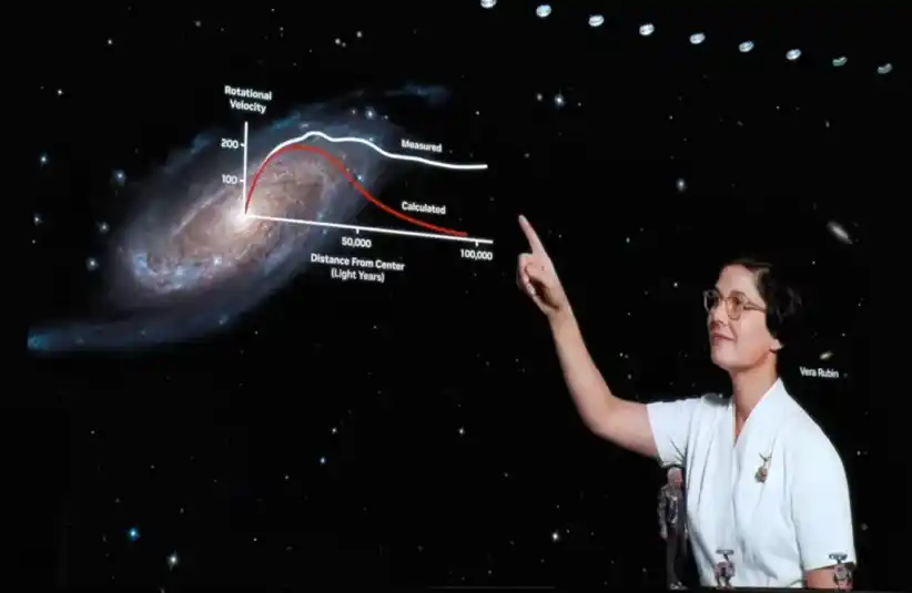 A picture of Vera Rubin as she points at a spiral galaxy on a starry background with superimposed graph lines labeled "Measured" and "Calculated" velocities. The scene feels educational as they learn about what she did by NVIDIA CEO Jensen Huang speaking live at CES 2026