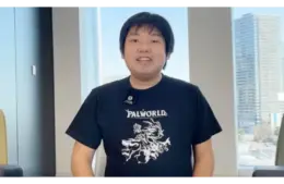 Poketpair CEO, Takuro Microbe, in a Palworld t-shirt, smiles in a bright office with urban buildings visible through large windows. The atmosphere is casual and friendly.