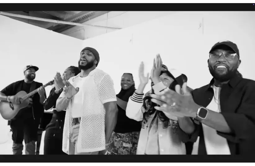 Darrel Walls & PJ Morton, and a diverse group of joyful people clapping along to music; one plays a guitar. The scene conveys a lively, upbeat, and communal atmosphere.