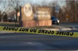 Crime scene tape creates a barrier in front of a blurred outdoor scene featuring a parked car and a sign. The atmosphere feels tense and serious. Recently, a fake ice agent robbed a home.