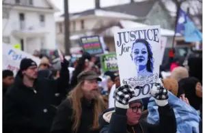 A diverse group of protesters holds signs, including one reading "Justice for Good," in a winter setting. The mood is determined and focused. Showing support in Minneapolis for Renee Nicole Good's death and leading towards her GoFundMe fundraiser.