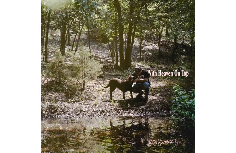 Zach Bryan album cover for With Heaven on Top depicting a man with his dog at the edge of a body of water.