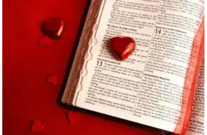 Open Bible on a red surface, displaying the "Love is the Greatest Gift" passage, surrounded by shiny heart-shaped candies, conveying warmth and love., Saint Valentine, Valentine's Day