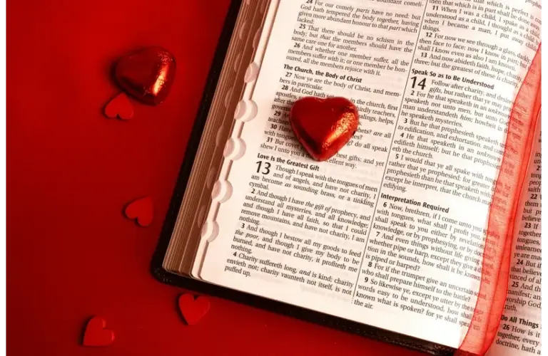 Open Bible on a red surface, displaying the "Love is the Greatest Gift" passage, surrounded by shiny heart-shaped candies, conveying warmth and love., Saint Valentine, Valentine's Day