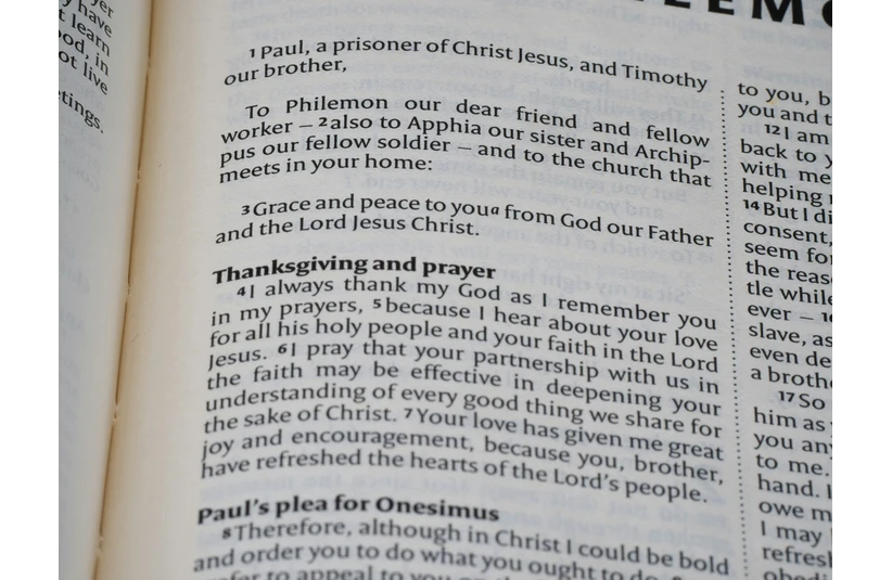 Open Bible page showing verses from the Book of Philemon. The text discusses grace, peace, Thanksgiving, and prayer, conveying a serene and reflective tone.