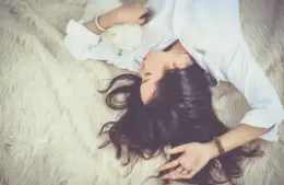 Image of Woman with long dark hair lies relaxed on a fluffy rug, holding a small white puppy. She wears a white shirt, conveying a peaceful, cozy atmosphere dreaming about old friends