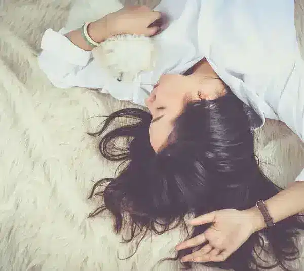 Image of Woman with long dark hair lies relaxed on a fluffy rug, holding a small white puppy. She wears a white shirt, conveying a peaceful, cozy atmosphere dreaming about old friends