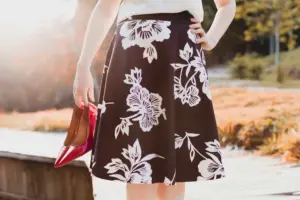 A person wearing a floral skirt holds red high heels represents spring fashion trends.