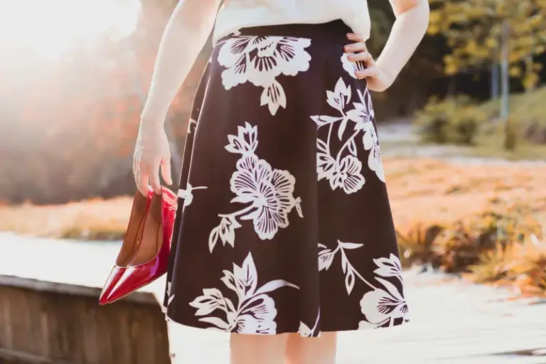 A person wearing a floral skirt holds red high heels represents spring fashion trends.