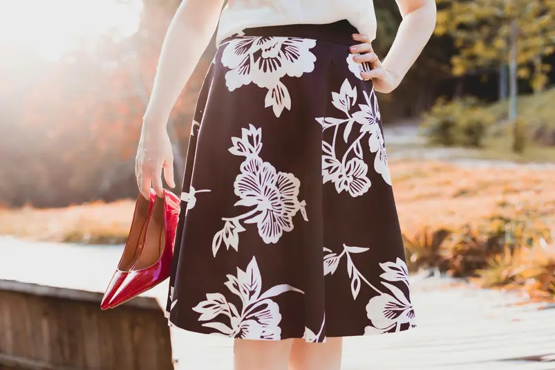 A person wearing a floral skirt holds red high heels represents spring fashion trends.