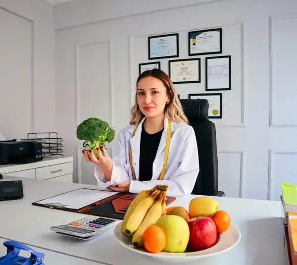 Dietician sitting behind a white desk and holding a large broccoli, clinicians guiding about viral diets