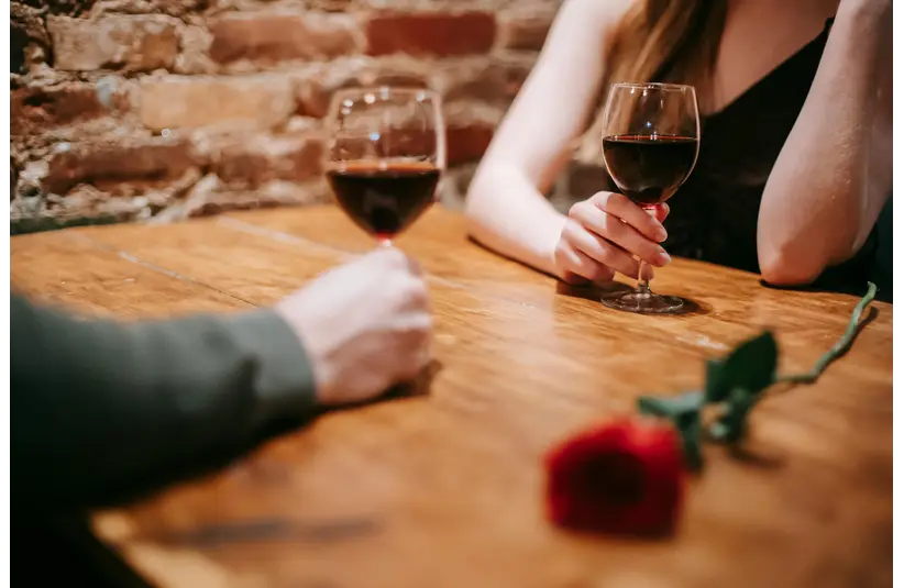 Photo of a couple at a restaurant enjoying two glasses of wine, with a rose on the table