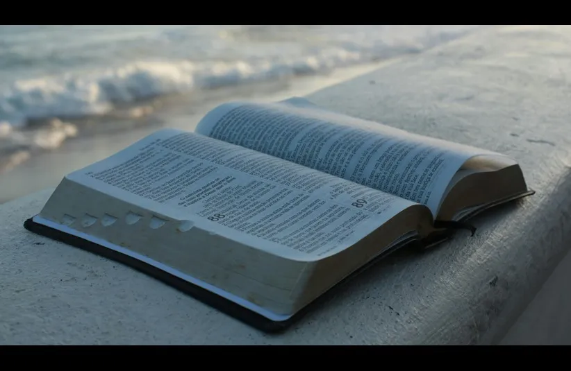 In daily devotion, an open Bible is set near a seashore. It may be open to the book of Job.