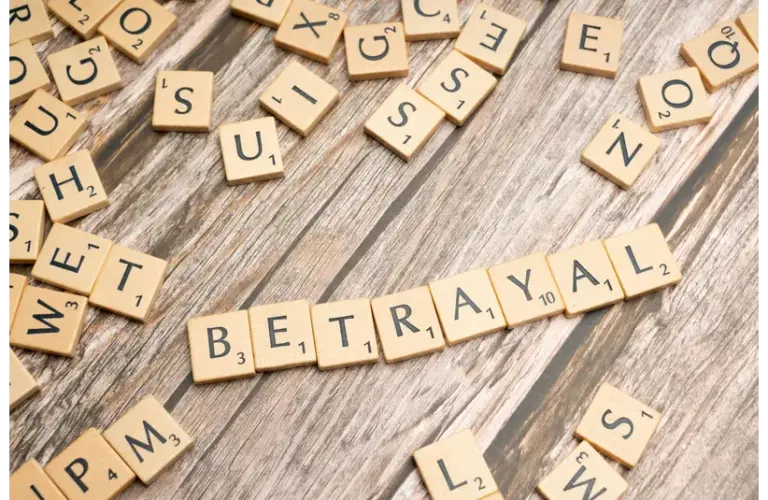 Wooden letter tiles spelling 'Betrayal' on a rustic wooden surface, conveying themes of deceit and dishonesty, representing cheating in relationships.