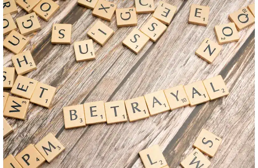 Wooden letter tiles spelling 'Betrayal' on a rustic wooden surface, conveying themes of deceit and dishonesty, representing cheating in relationships.