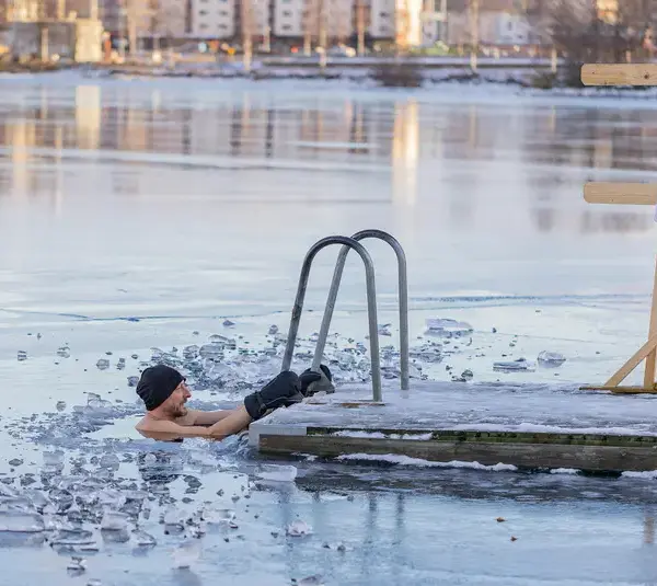 A man wearing a hat and gloves swims in an icy lake following cold plunging trend