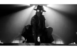 Spider-Noir crouches in dramatic black-and-white lighting. Circular glasses and a mask add intrigue; a tense, shadowy atmosphere.