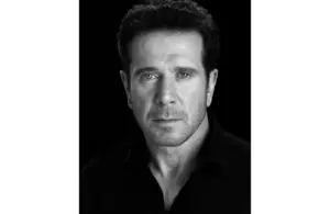 A Black and white portrait of Bobby J. Brown, a serious man with short dark hair, wearing a dark shirt, against a black background, conveying intensity and focus.