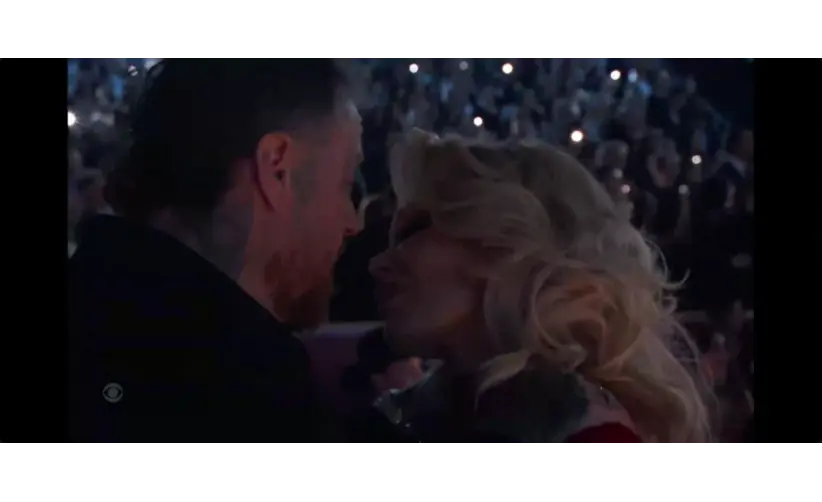 Jelly Roll and wife, Bunnie Xo, share an intimate moment at a crowded event. The audience in the background holds up lights, creating a romantic atmosphere.