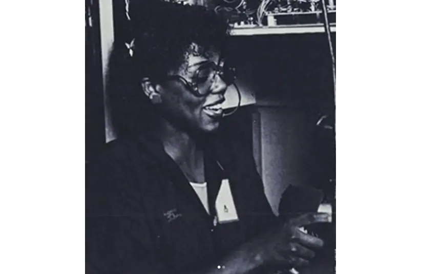 Black and white photo of a smiling Alice "Wonderwoman" Washington in glasses, working with electronic equipment. She appears focused and engaged, conveying a sense of purpose.