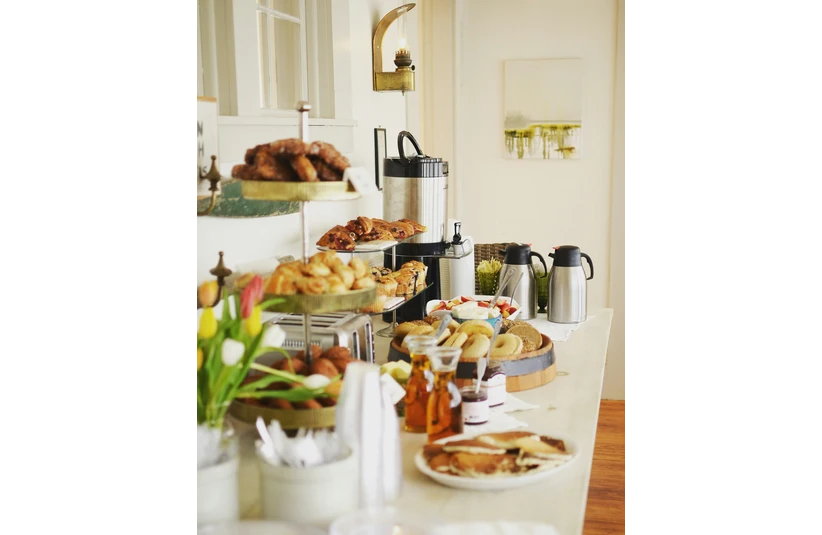 A buffet table with pastries, bagels, and fruit, alongside coffee and tea dispensers. Bright tulips add color, creating a warm, inviting atmosphere. Continental breakfast, hotel breakfast