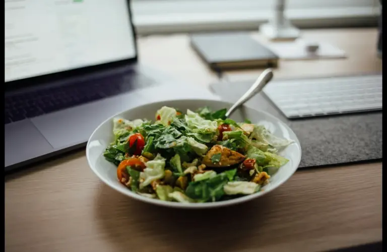 Lunch breaks for remote and hybrid workers, featuring a plate of vegetable salad next to a laptop