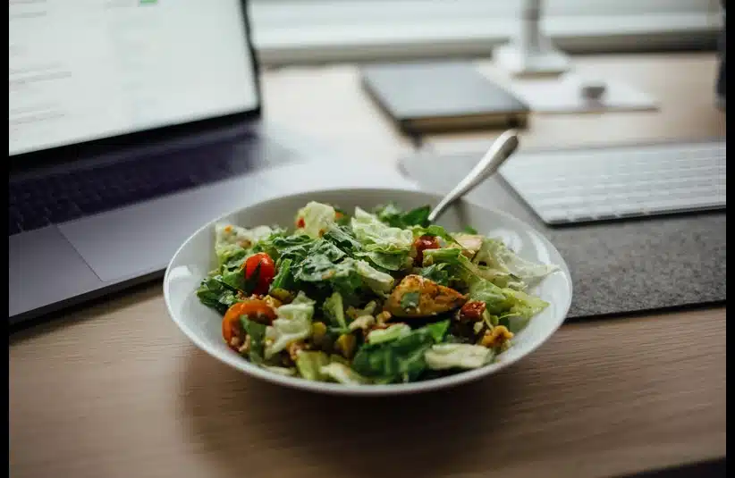 Lunch breaks for remote and hybrid workers, featuring a plate of vegetable salad next to a laptop