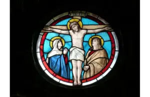Stained glass window depicting a crucifixion scene. Central figure on a cross with halo, flanked by two figures in robes. Blue and red hues convey solemnity. Lent, Christian, Catholic, church, Jesus