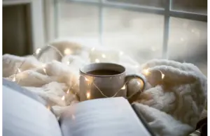 a cozy setting with a book, soft blanket, fairy lights, and a warm cup of coffee