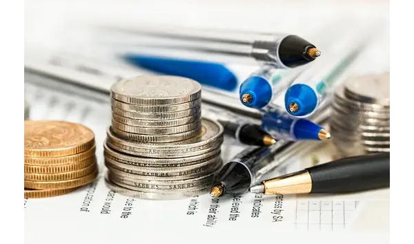 Stacks of silver and gold coins, a cluster of ballpoint pens, financial documents depicting financial realism and business planning