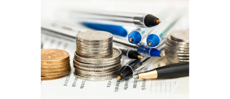 Stacks of silver and gold coins, a cluster of ballpoint pens, financial documents depicting financial realism and business planning