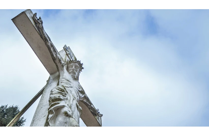 A weathered stone crucifix with a detailed figure against a cloudy blue sky, conveying solemnity and spirituality. The angle emphasizes the statue's expression, Jesus, Good Friday