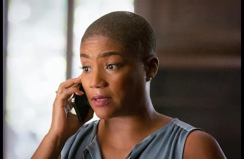Tiffany Haddish is show with a buzz cut and a gray V-neck making a phone call.