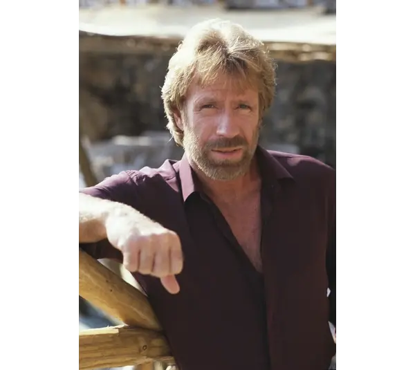 Image of Chuck Norris in a button down shirt with one arm propped up. He is squinting at the camera.