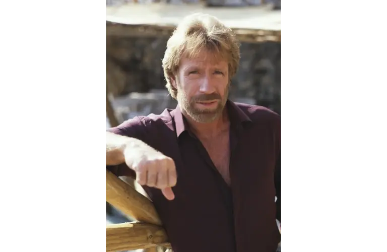 Image of Chuck Norris in a button down shirt with one arm propped up. He is squinting at the camera.