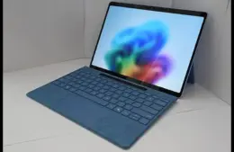 Microsoft Windows 11 Laptop. A sleek blue laptop with a detachable keyboard is open, displaying a vibrant, abstract, colorful wallpaper. It rests on a white surface, conveying a modern, tech-savvy tone.