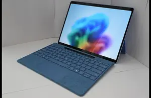 Microsoft Windows 11 Laptop. A sleek blue laptop with a detachable keyboard is open, displaying a vibrant, abstract, colorful wallpaper. It rests on a white surface, conveying a modern, tech-savvy tone.