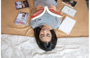 A woman laying down with books laid out on a bed, reading.