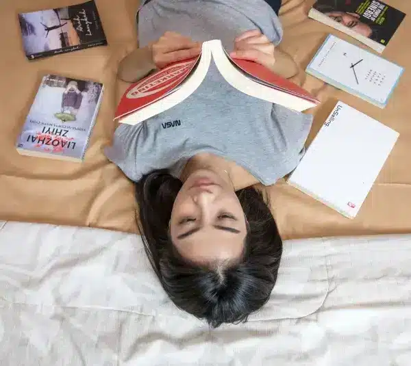 A woman laying down with books laid out on a bed, reading.