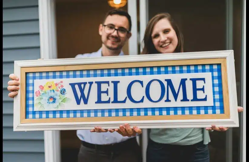 In daily devotion, a man and woman hold up a welcome sign.
