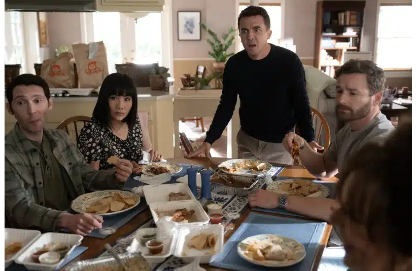 The cast of "Malcolm In The Middle: Life's Still Unfair" sit around a dining table with takeout containers, looking surprised. The mood is tense, and they appear to be mid-conversation.