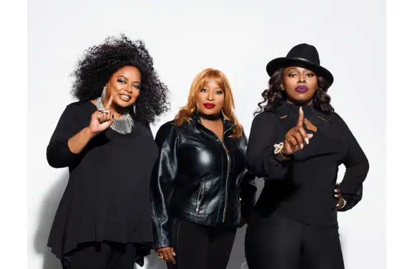 The Sequence pose confidently against a white background. They wear black outfits, with one in a leather jacket and another in a hat, all holding up one finger.