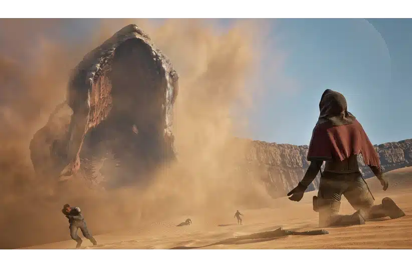 A massive sand worm emerges from the desert in Dune: Awakening, creating a dust storm. People in cloaks flee in fear under a clear blue sky, conveying urgency and danger.