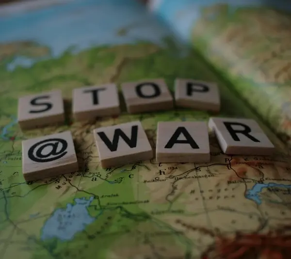 Scrabble tiles spell "STOP @ WAR" on a detailed world map. The message is clear and urgent, advocating for peace against the backdrop of geopolitical regions. Trapped in GWOT.