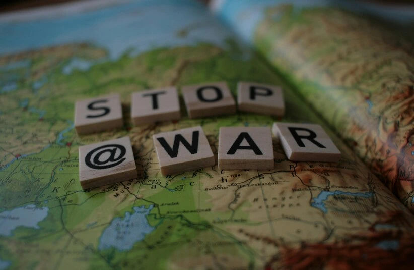 Scrabble tiles spell "STOP @ WAR" on a detailed world map. The message is clear and urgent, advocating for peace against the backdrop of geopolitical regions. Trapped in GWOT.
