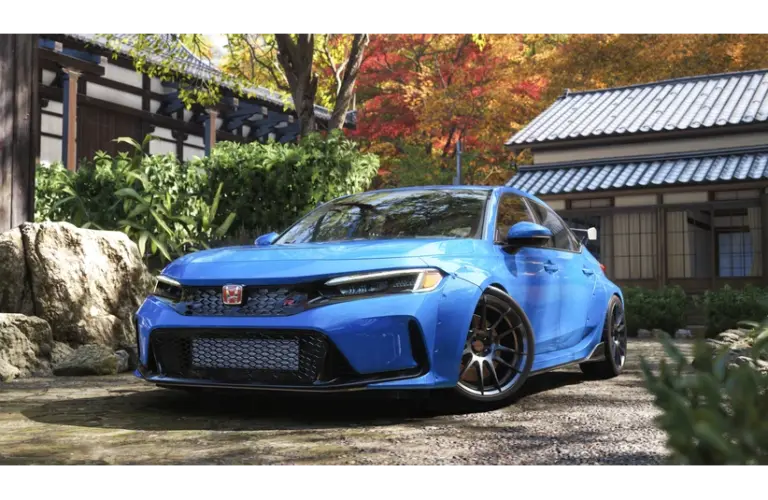 Forza Horizon 6 a Blue sporty car parked in a tranquil Japanese garden with stone path, lush greenery, and a traditional building. Vibrant autumn leaves enhance the serene setting.