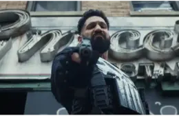 Frank Castle, The Punisher, with a stern expression, points a gun towards the camera, wearing tactical gear. He's set against an old, vintage restaurant sign. The mood is tense.